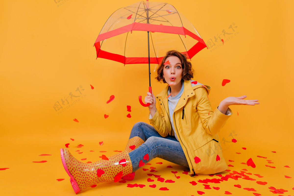 雨穿着胶鞋和蓝色牛仔裤 打着伞的漂亮女孩的室内照片坐在地板上的快乐女士的画像 红色的纸心天气漂亮情绪