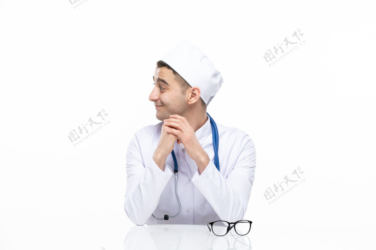 观点正面图：年轻的医生穿着医疗服坐在桌子后面微笑年轻医生医学