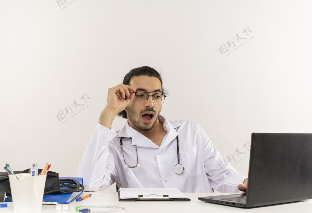 工作惊讶的年轻男医生戴着医用眼镜 穿着带听诊器的医用长袍年轻男性惊喜