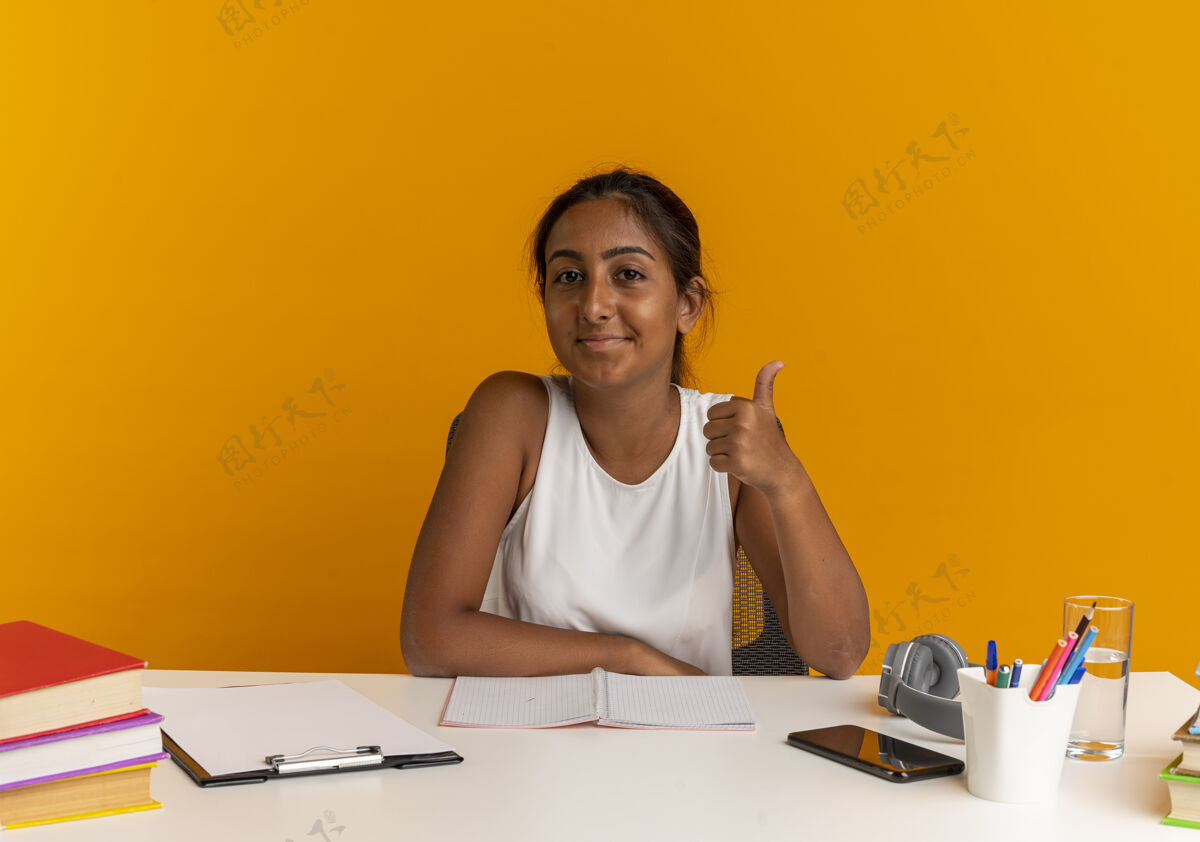 拇指坐在书桌旁 手里拿着学习用具的小女孩高兴地把大拇指放在橘子上工具年轻请