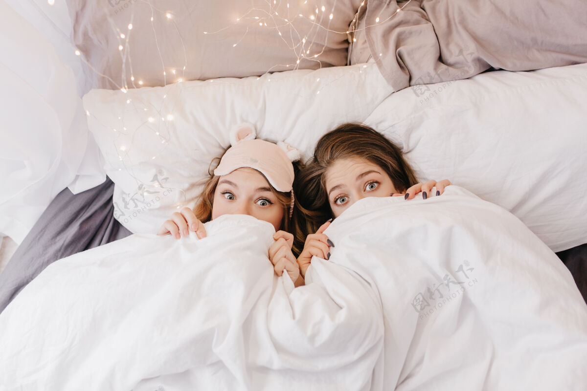 朋友有趣的年轻女孩躲在毯子下室内照片的情感姐妹在上午的乐趣拍照醒着年轻女人