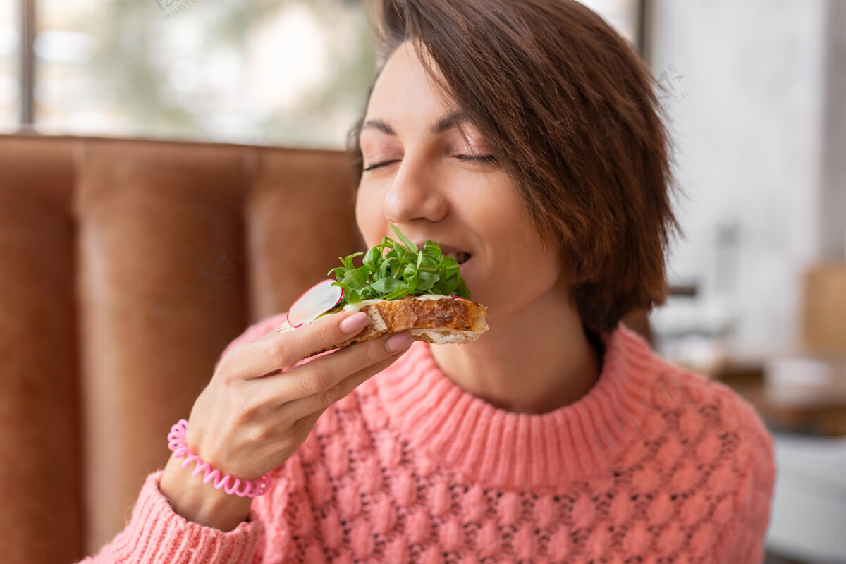 健康一位女士穿着一件温暖舒适的毛衣在一家餐厅享用健康的早餐 烤面包配芝麻菜和三文鱼享受切片肖像