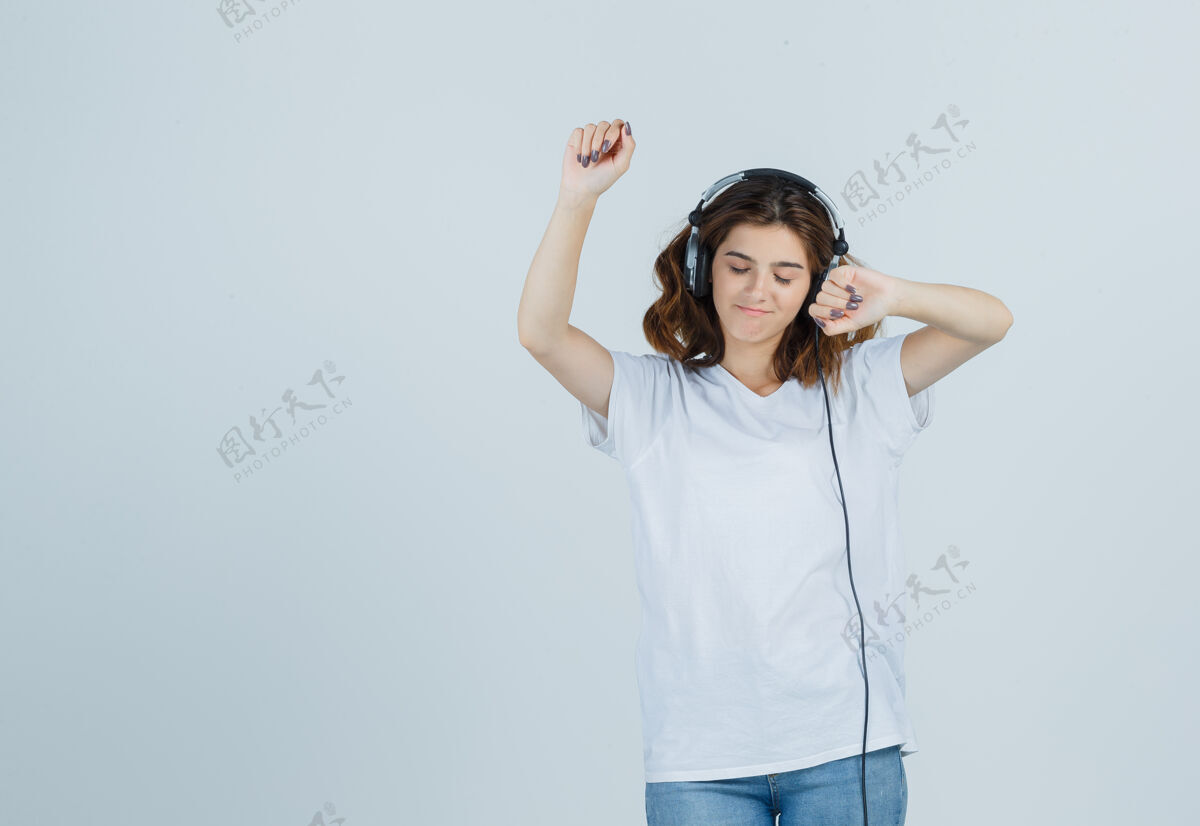 女性穿着白色t恤 牛仔裤的年轻女性 戴着耳机欣赏音乐 看起来很活泼 正面视图女人年轻活泼