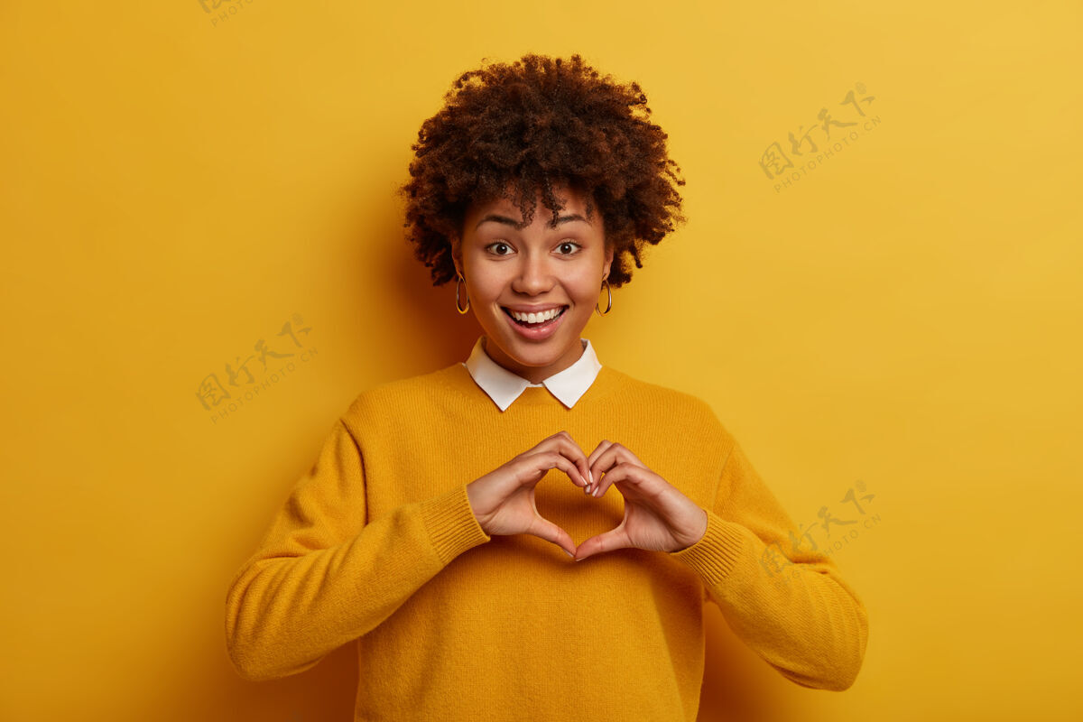 凝视浪漫的概念很高兴女孩用手做心形符号 穿休闲套头衫 向男友表白爱意 穿黄色整洁的套头衫 开心地微笑志愿者有社会责任感单色显示请