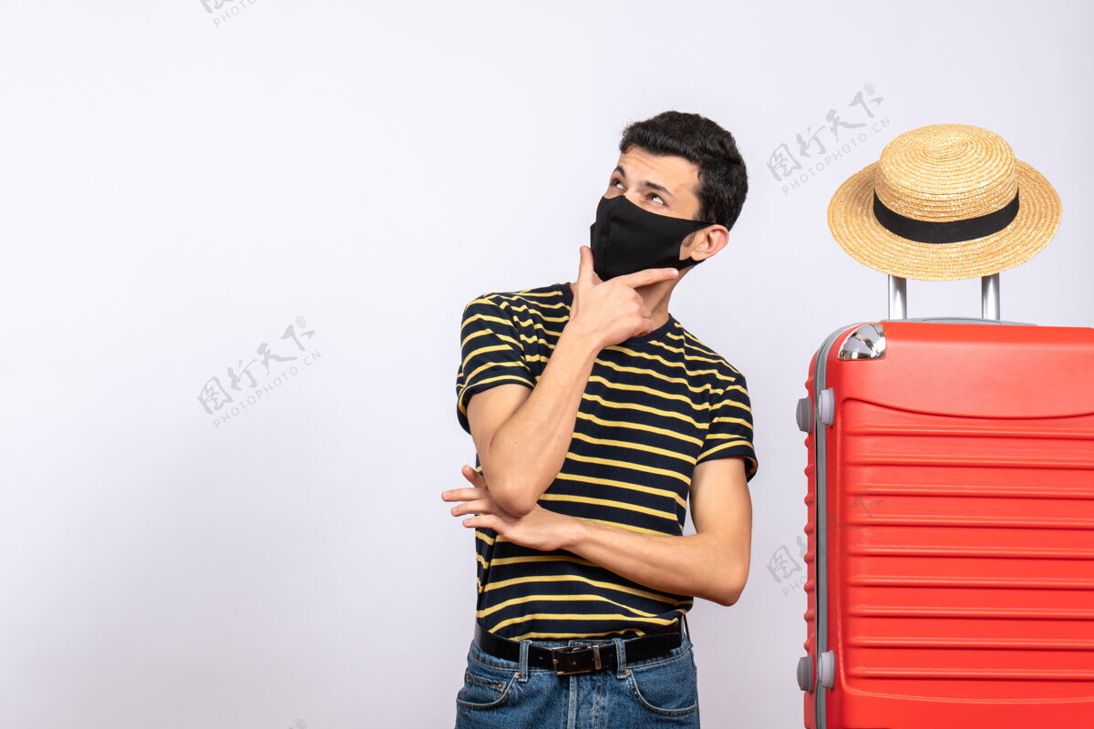 时尚正面图：站在红色手提箱旁的戴着黑色面具的年轻游客激动不已站立头发成人