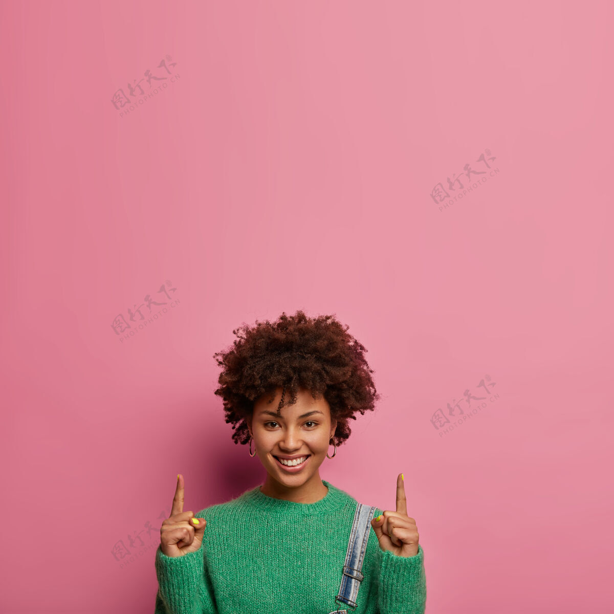 高兴容貌讨人喜欢的女人邀请上楼 向上指食指 展示哪里有最好的折扣 穿绿色毛衣 模特靠着玫瑰色的墙壁 做广告指标指向请