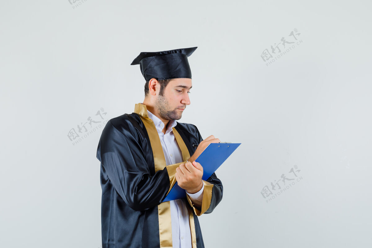 模特年轻人穿着毕业制服在剪贴板上做笔记 看上去很忙正视图剪贴板欢呼成功