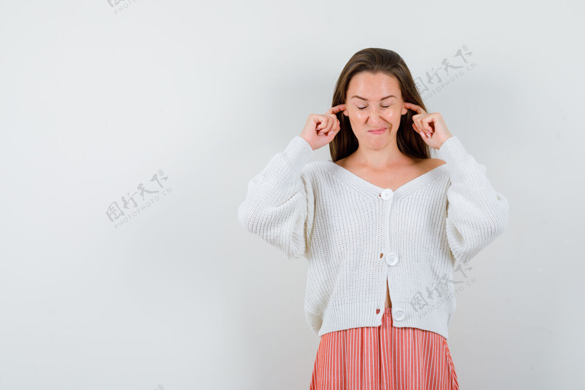 开衫年轻女性用手指塞住耳朵 穿着开衫和裙子 显得无聊孤立女人成人微笑