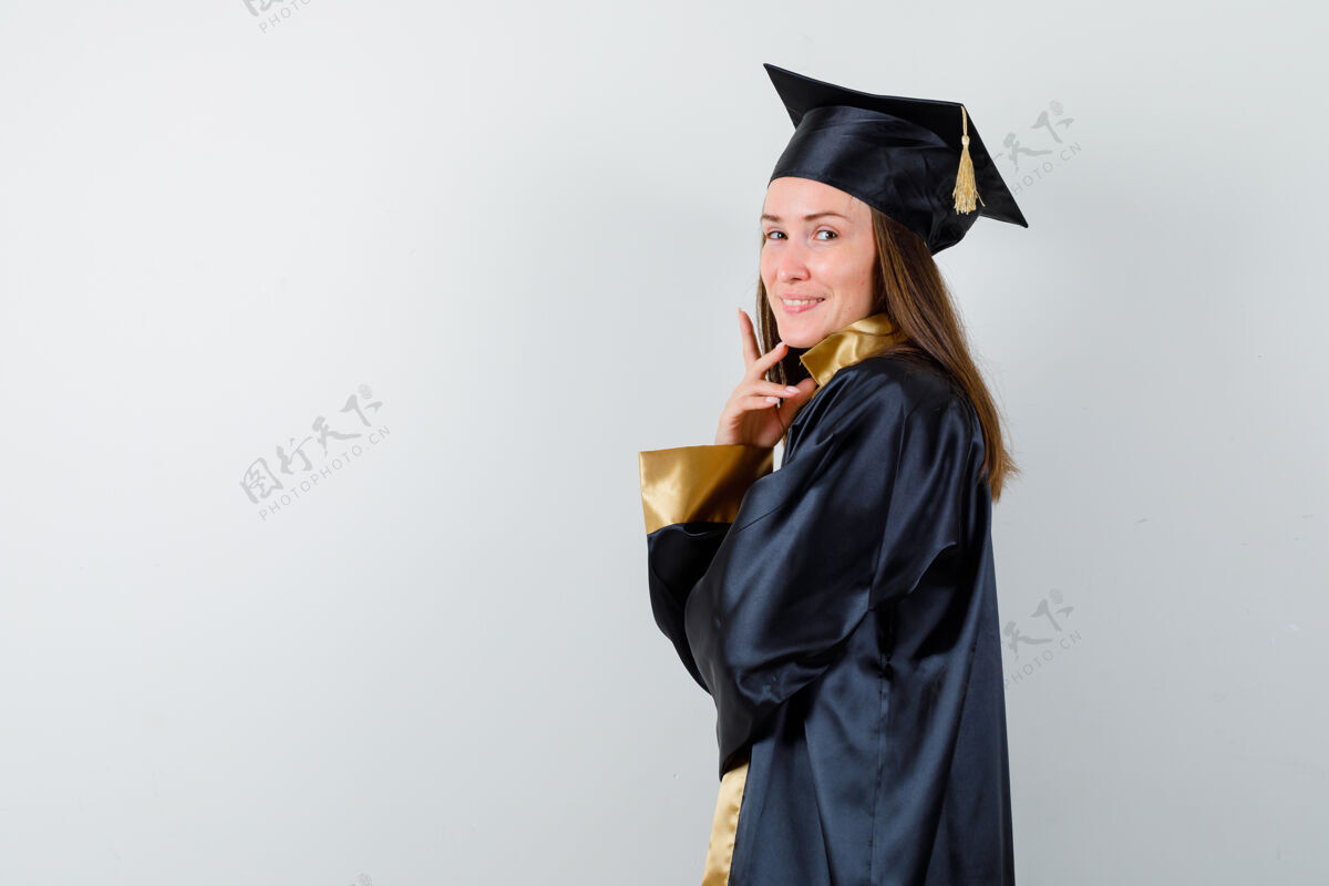 衣服年轻的女毕业生穿着学院服站在那里而漂亮女人