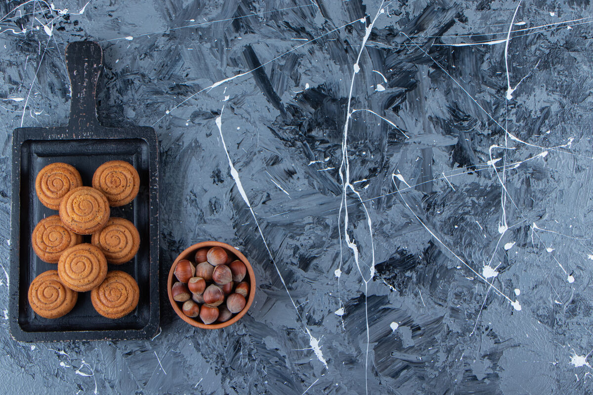 圆形一块黑色的木板 上面放着新鲜甜甜的圆形饼干和健康的坚果 背景是大理石食物零食面粉