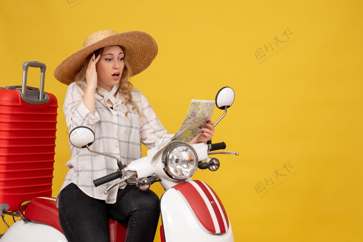 人年轻女子戴着帽子 坐在摩托车上看地图 脸上泛着困惑的黄色压抑年轻女子坐比赛