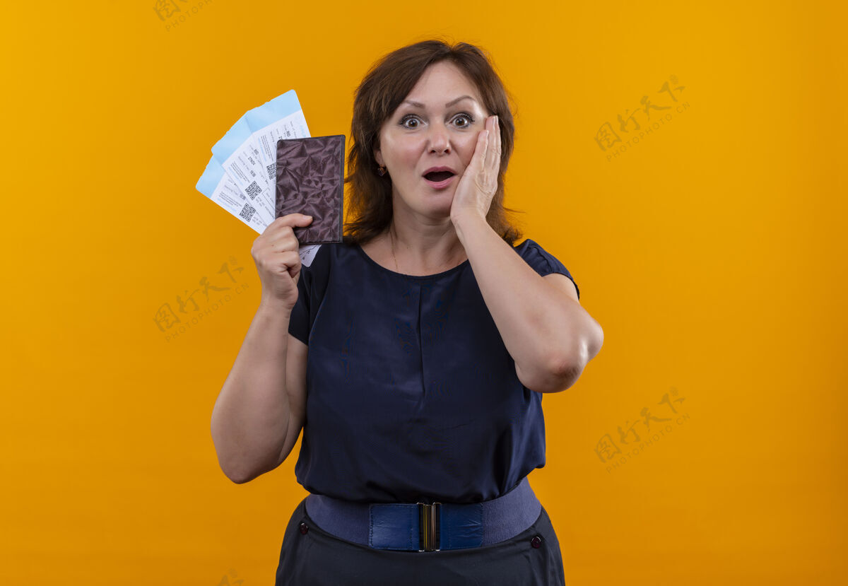 女人惊讶的中年旅游女拿着机票和钱包把手放在脸颊上脸颊票手势
