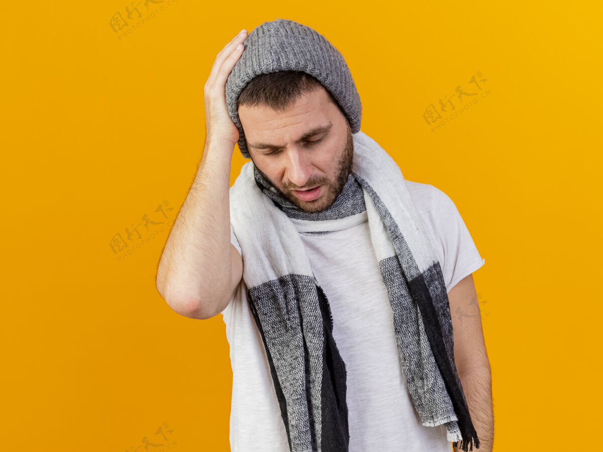 年轻闭上眼睛 戴着冬帽 戴着围巾 手放在疼痛的头上 隔离在黄色背景上的年轻病人头围巾手