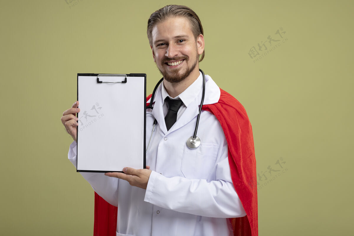举行带着微笑的年轻超级英雄戴着听诊器 穿着医用长袍 拿着剪贴板 背景是橄榄绿橄榄长袍家伙