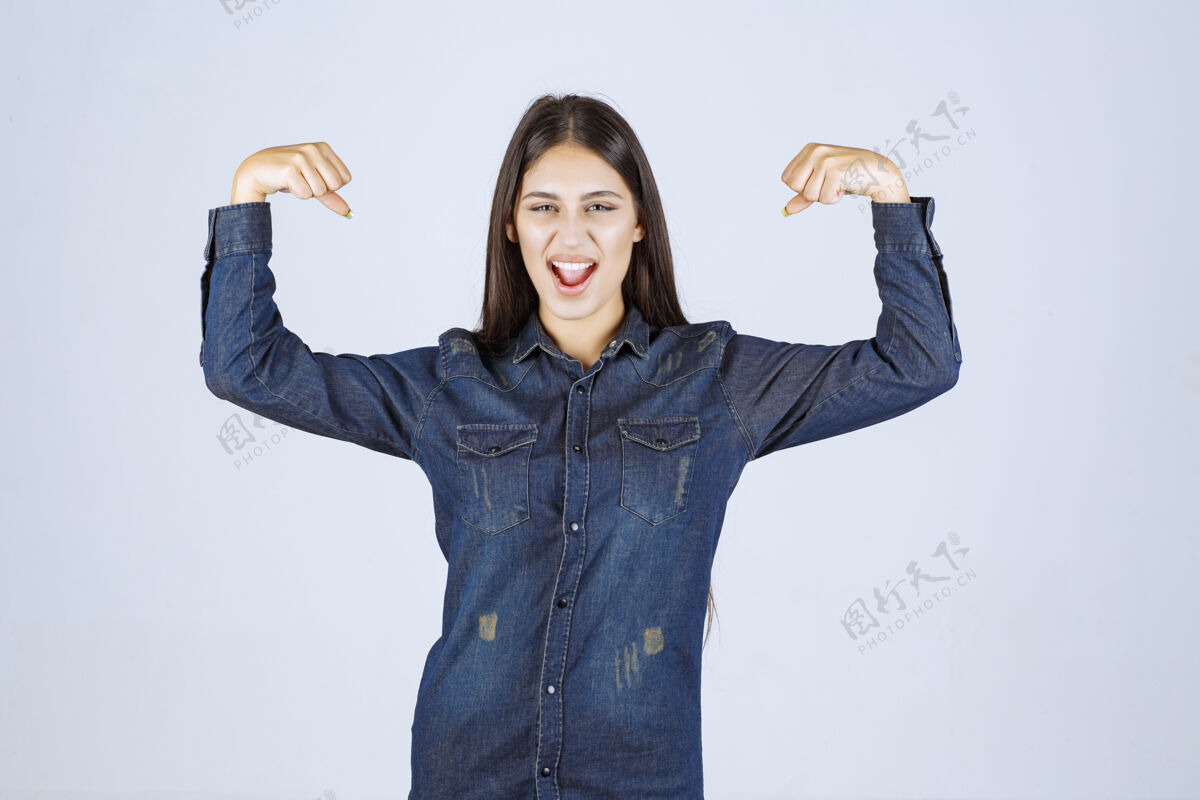 女人穿着牛仔衬衫的年轻女子展示了她的手臂肌肉人力量锻炼