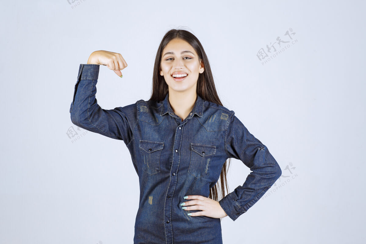 锻炼穿着牛仔衬衫的年轻女子展示了她的手臂肌肉聪明休闲年轻