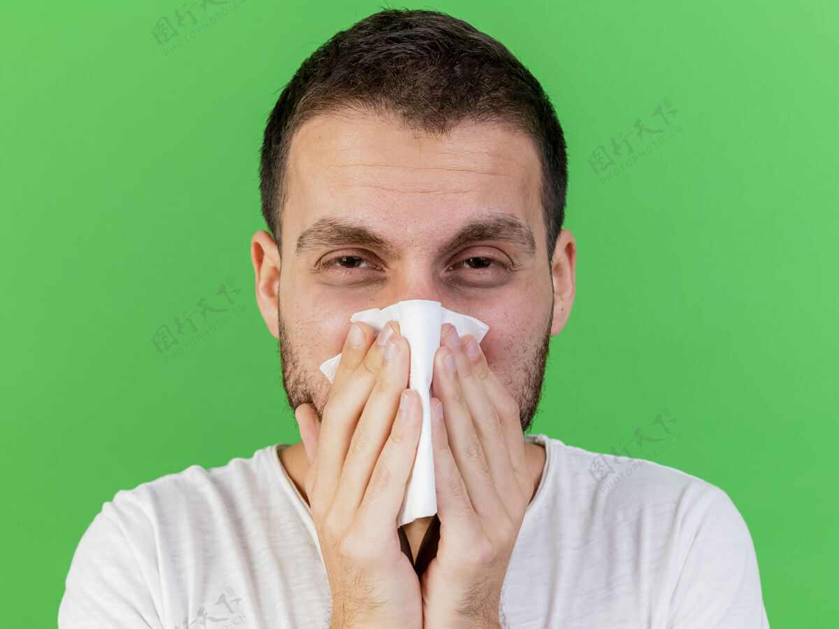 湿巾看着镜头 年轻的病夫用隔离在绿色背景上的餐巾擦鼻子相机鼻子餐巾