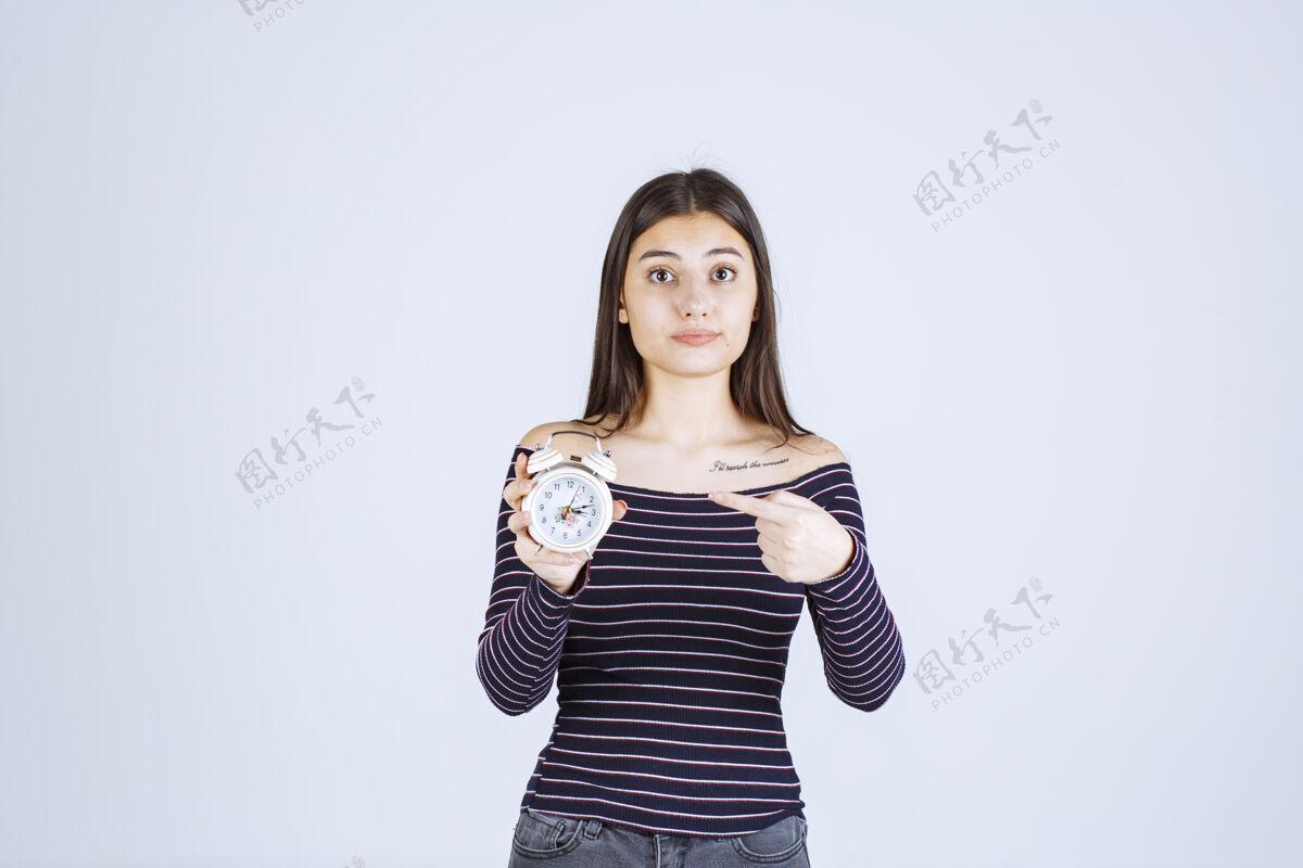 女售货员穿着条纹衬衫的女孩手里拿着闹钟 把它当作一种新产品来推销职员人体模特销售