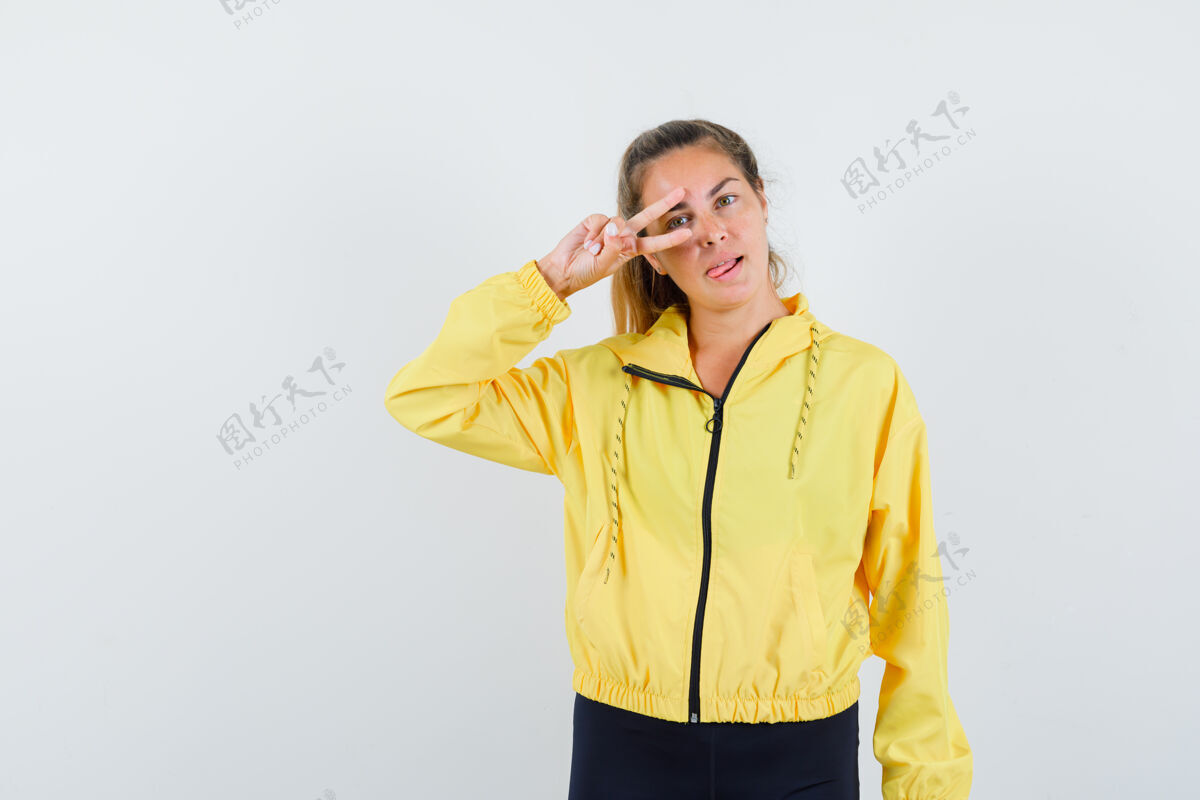 模特一个金发女人眼睛上有v字 穿着黄色棒球服和黑色裤子伸出舌头 看起来很严肃严肃裤子干净