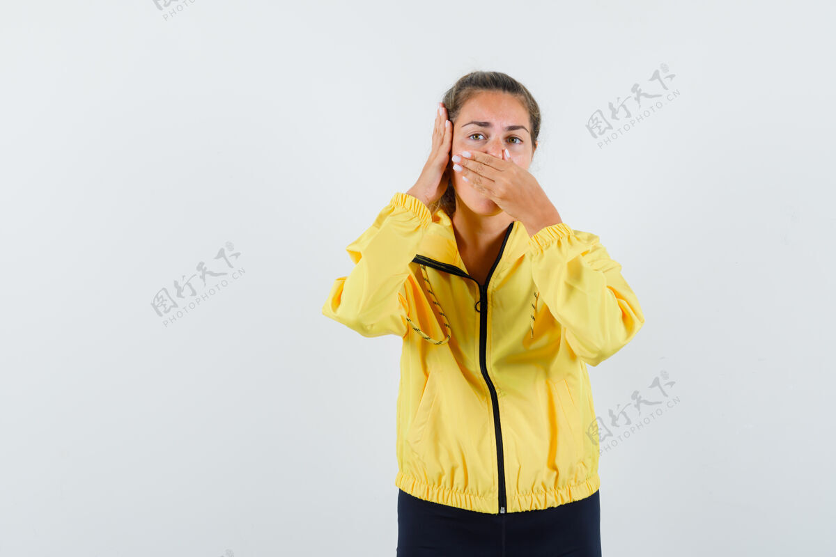 女人年轻女子捏鼻子由于臭味和按在耳朵上的手在黄色的棒球服和黑色裤子 看起来烦躁可爱坏头发