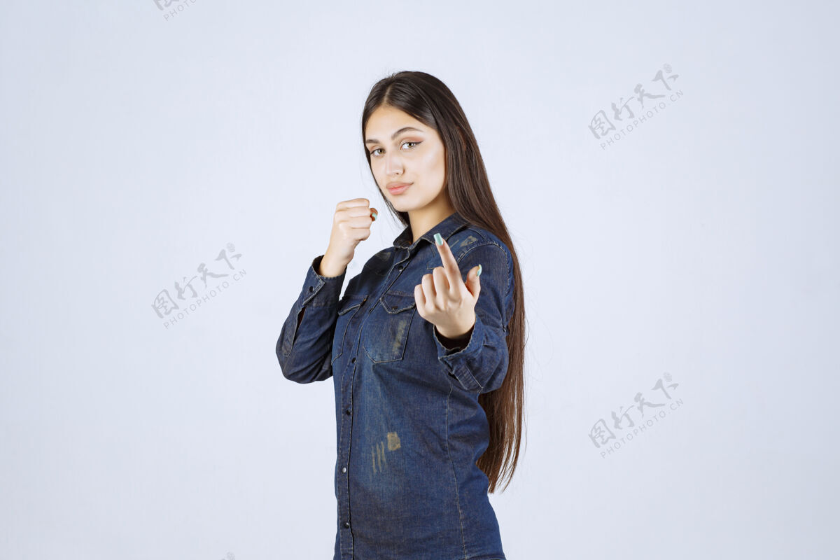 休闲穿着牛仔衫的年轻女子指着她面前的人姿势年轻女性