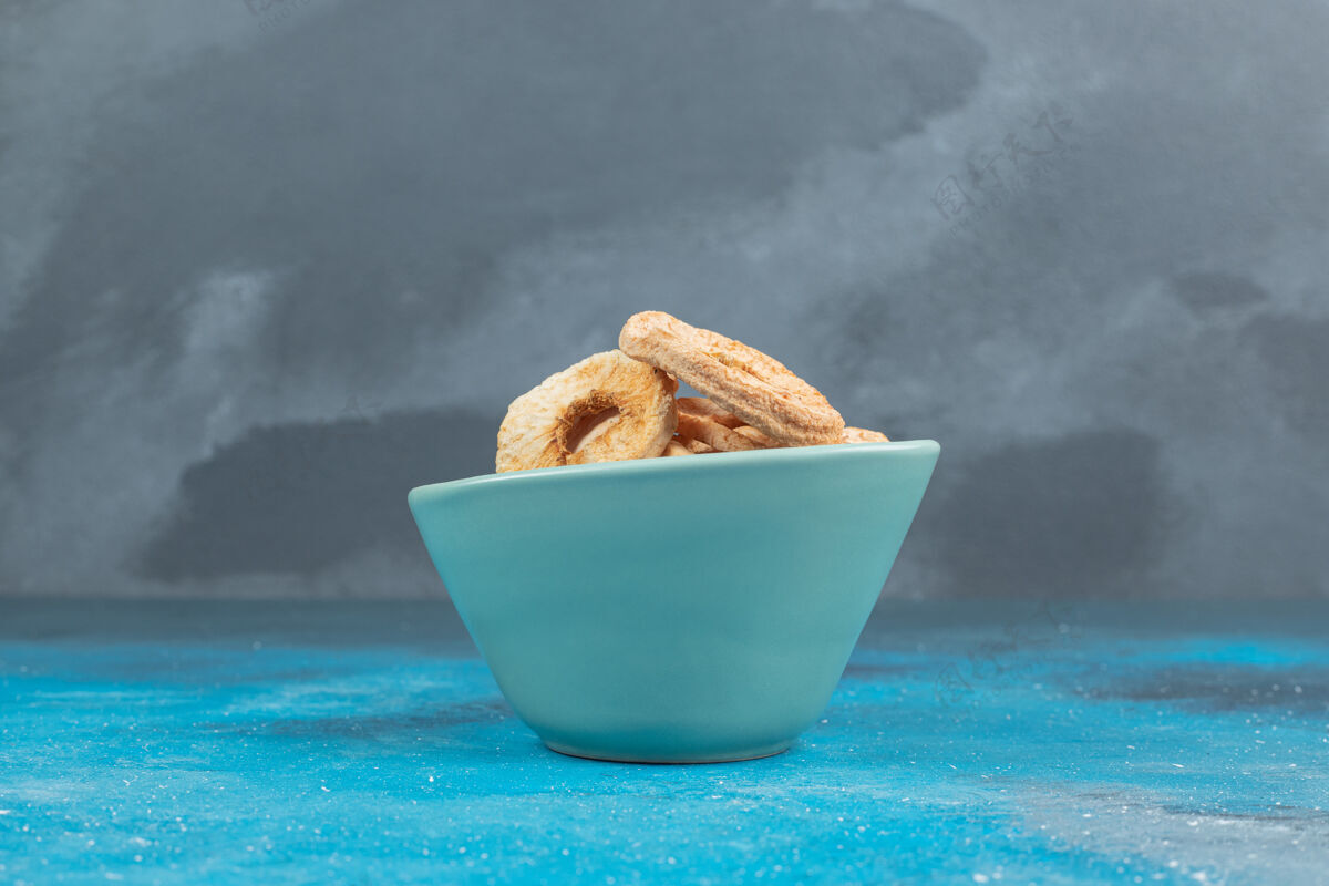 甜点蓝色表面上的一碗干苹果圈切片零食薯片