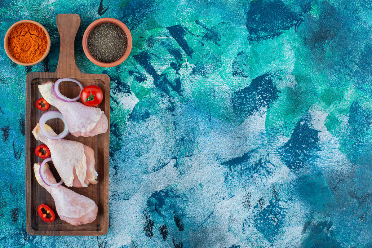 蛋白质生鸡腿和蔬菜放在一块板上 蓝色背景板洋葱番茄