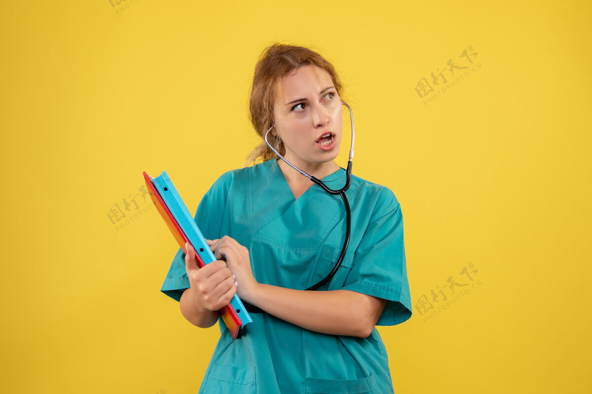 健康黄色墙壁上穿着医疗服的女医生的正视图 带有分析和听诊器微笑护士医疗
