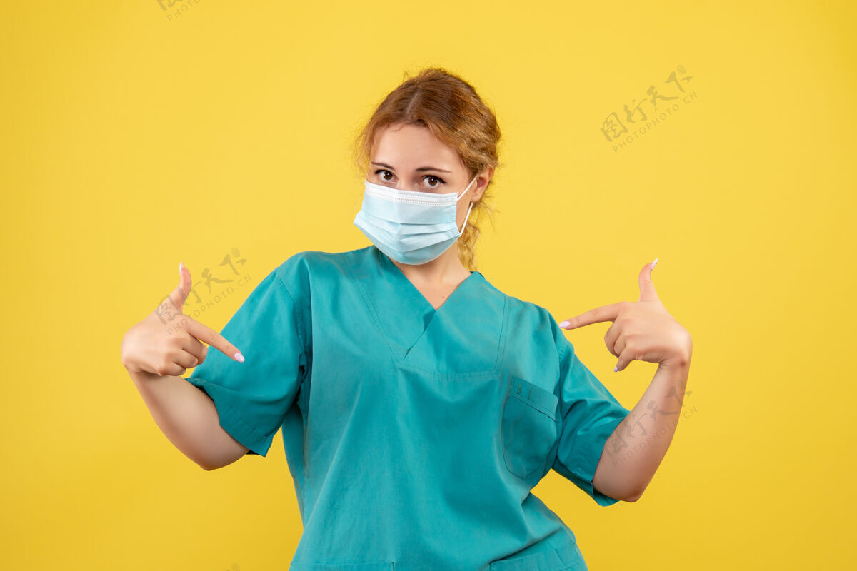 女医生黄色墙壁上穿着医疗服 戴着口罩的女医生的正视图健康人大流行