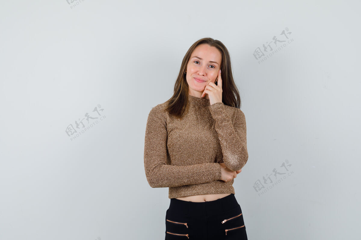 人年轻女子穿着金色的毛衣和黑色的裤子站在思考的姿势 看起来很高兴站立头发年轻