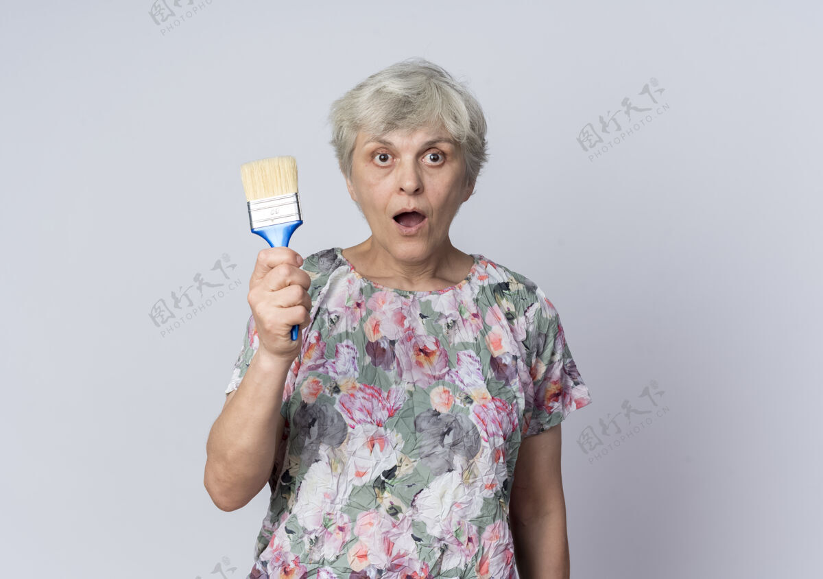 老人震惊的老妇人拿着油漆刷隔离在白墙上刷子老人老人
