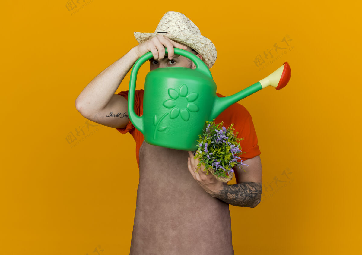 通过年轻的男园丁戴着园艺帽 把花放在花盆里 透过浇水罐看园艺橘子穿