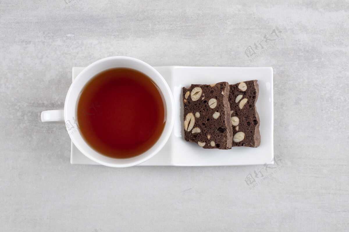 饼干自制巧克力布朗尼和一杯茶放在碟子上 放在大理石桌上甜点糕点杯子