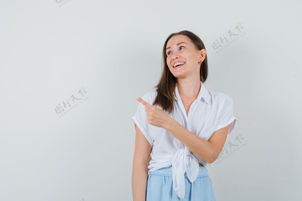 头发一个穿着白衬衫和浅蓝色裙子的年轻女人用食指指着左边 看上去很高兴欢呼成人快乐