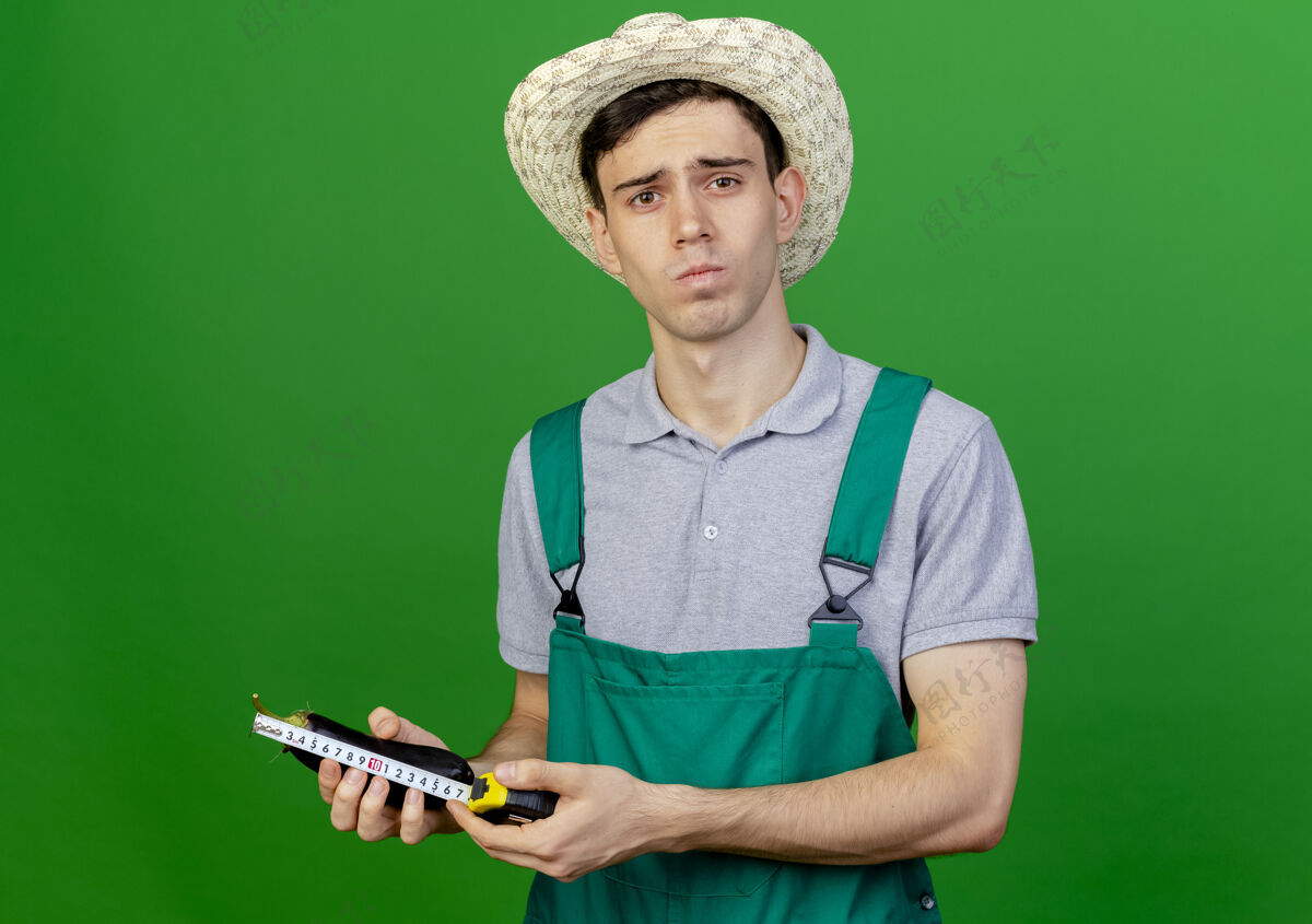 绿色自信的年轻男园丁戴着园艺帽用卷尺量茄子空间花园信心
