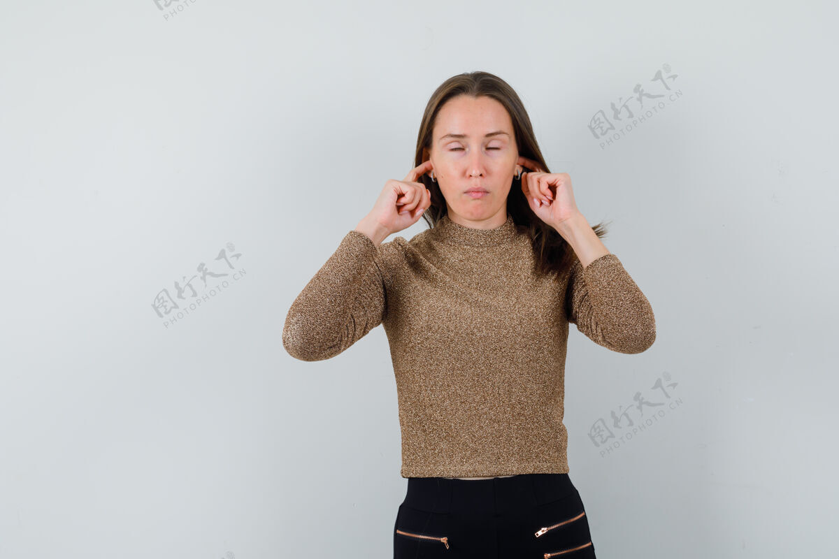 黑发穿金色上衣的年轻女子用手指塞住耳朵 看上去很平静女人成人微笑