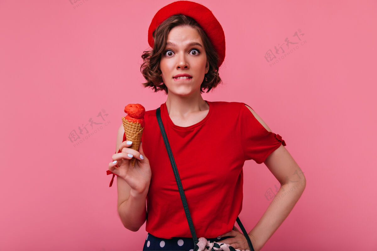 女人优雅的法国女孩 手拿冰激凌 修着白色指甲室内拍摄情绪化的黑发女士穿着红色衣服吃甜点贝雷帽室内美丽