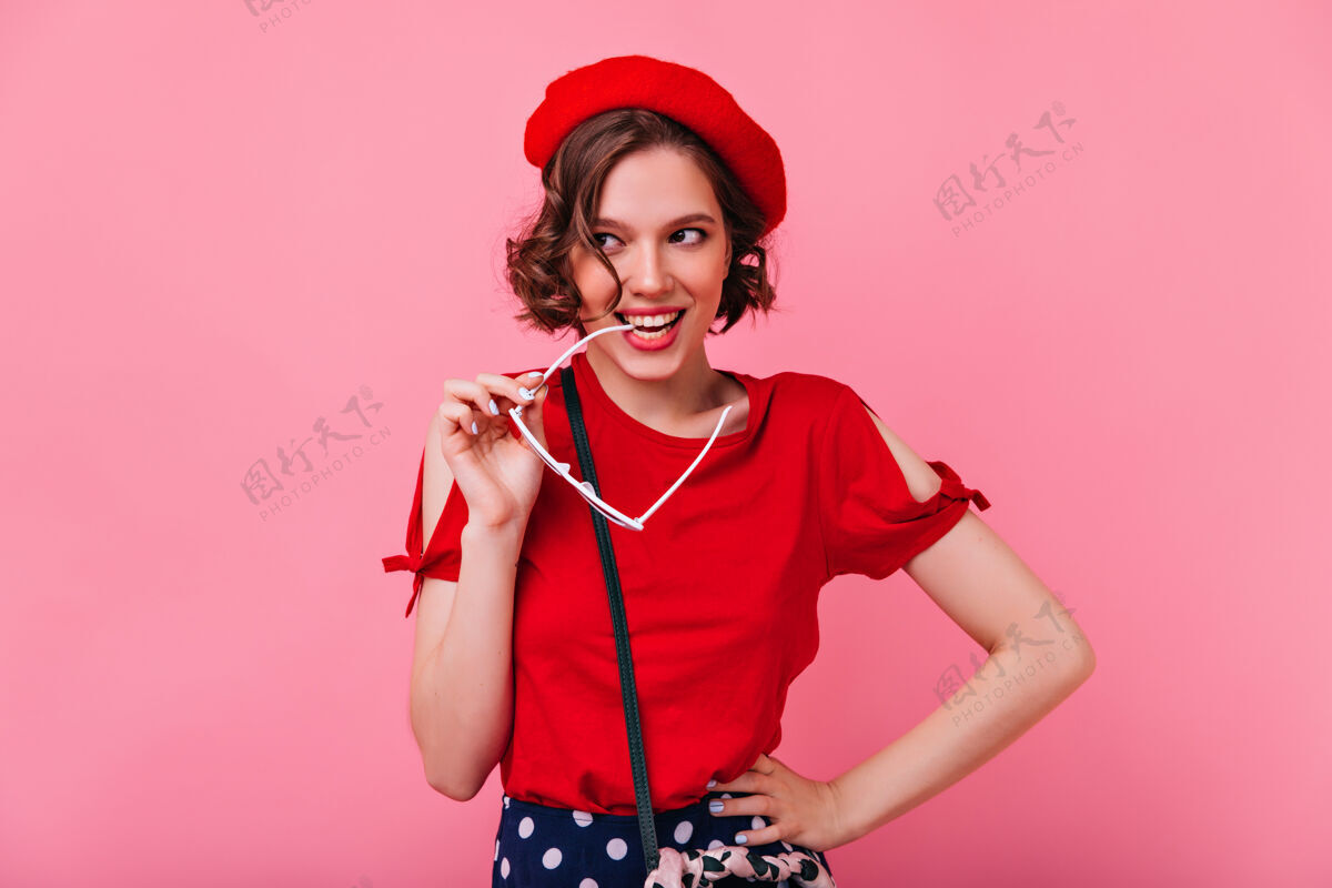 人物迷人的卷发女孩摆出俏皮的微笑室内拍摄的法国女士戴着红色贝雷帽 无忧无虑微笑帽子女性