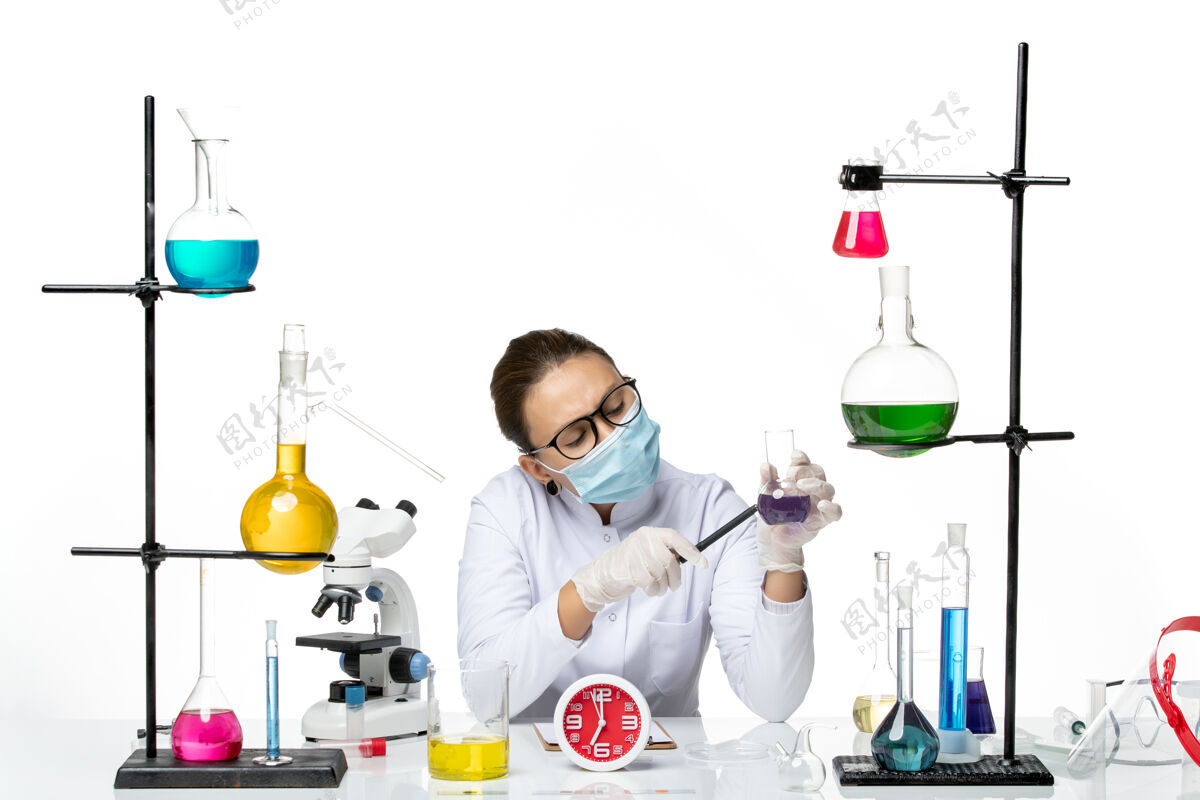 坐着前视图穿着医疗服的女化学家戴着面罩坐在一个白色背景上拿着一支笔溅实验室病毒化学冠状病毒化学实验喷溅