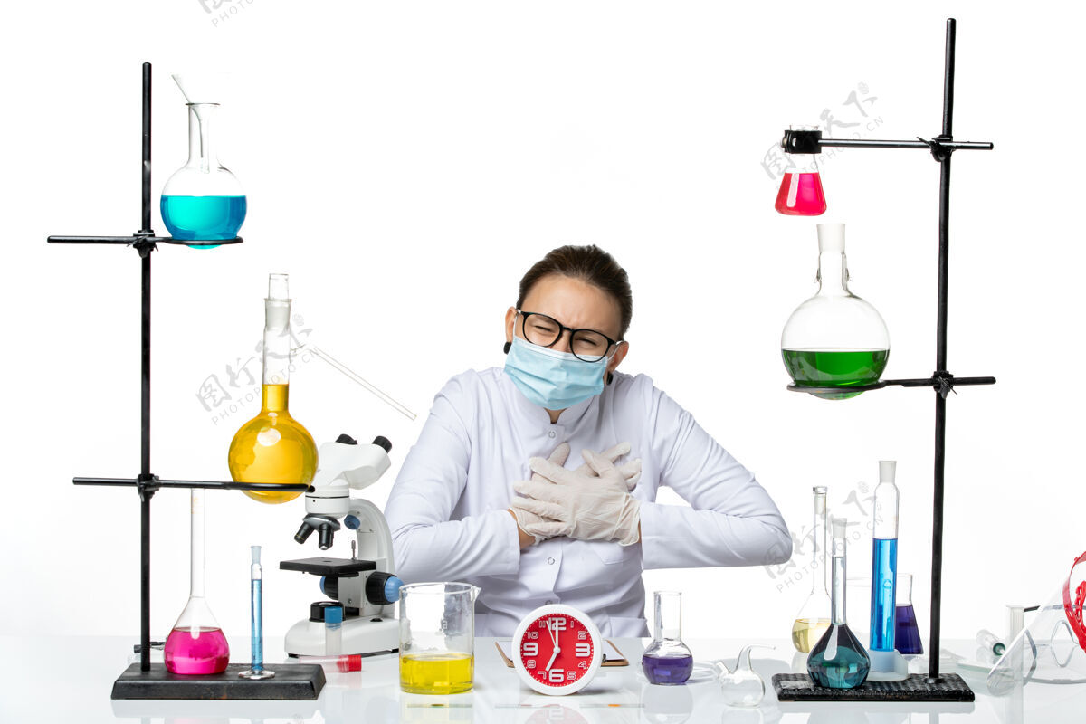 前面前视图穿着医疗服的女化学家带着面罩坐在白色背景上的溶液化学病毒实验室病毒-飞溅套装喷溅医生