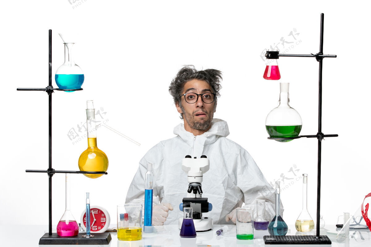 病毒前视图穿着特殊防护服的疯狂男科学家围坐在桌子旁 解决浅白色背景的实验室疾病病毒-科学病毒坐着实验室桌子