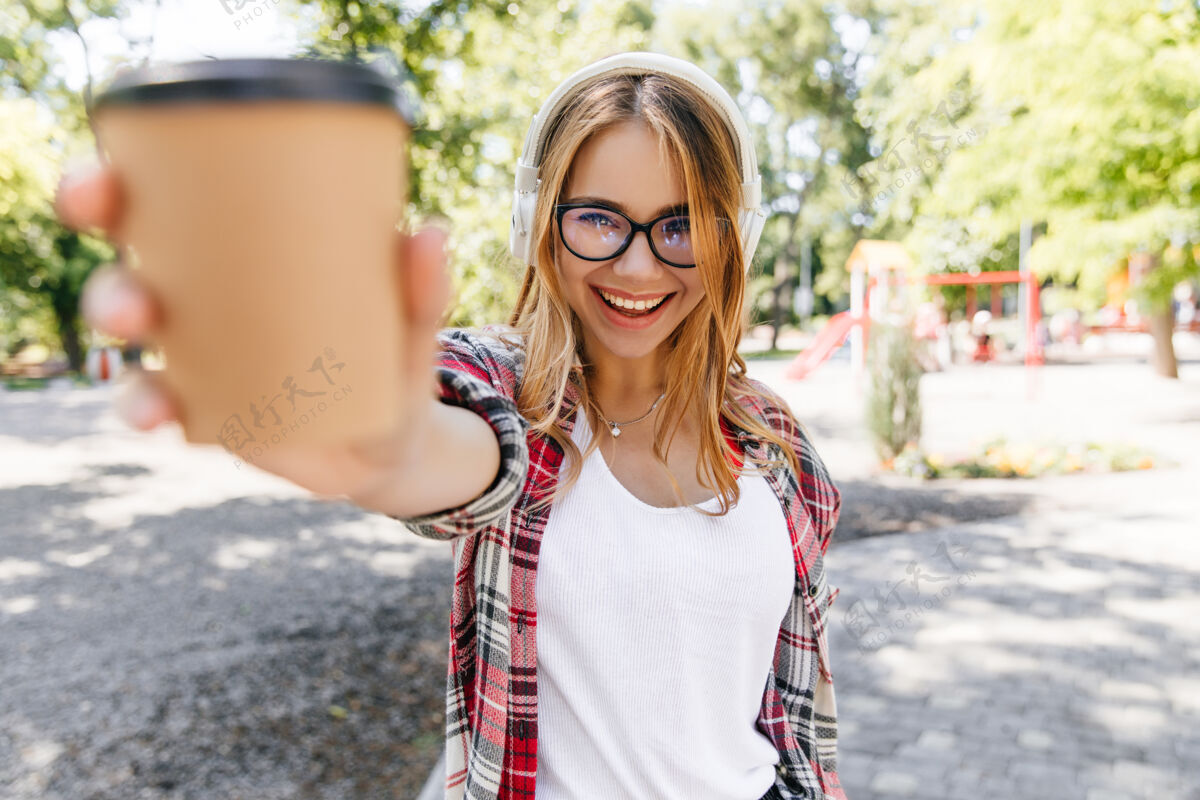 散步自信的微笑女孩在公园里摆姿势快乐的金发女士拿着一杯咖啡在大自然中乐趣女性放松
