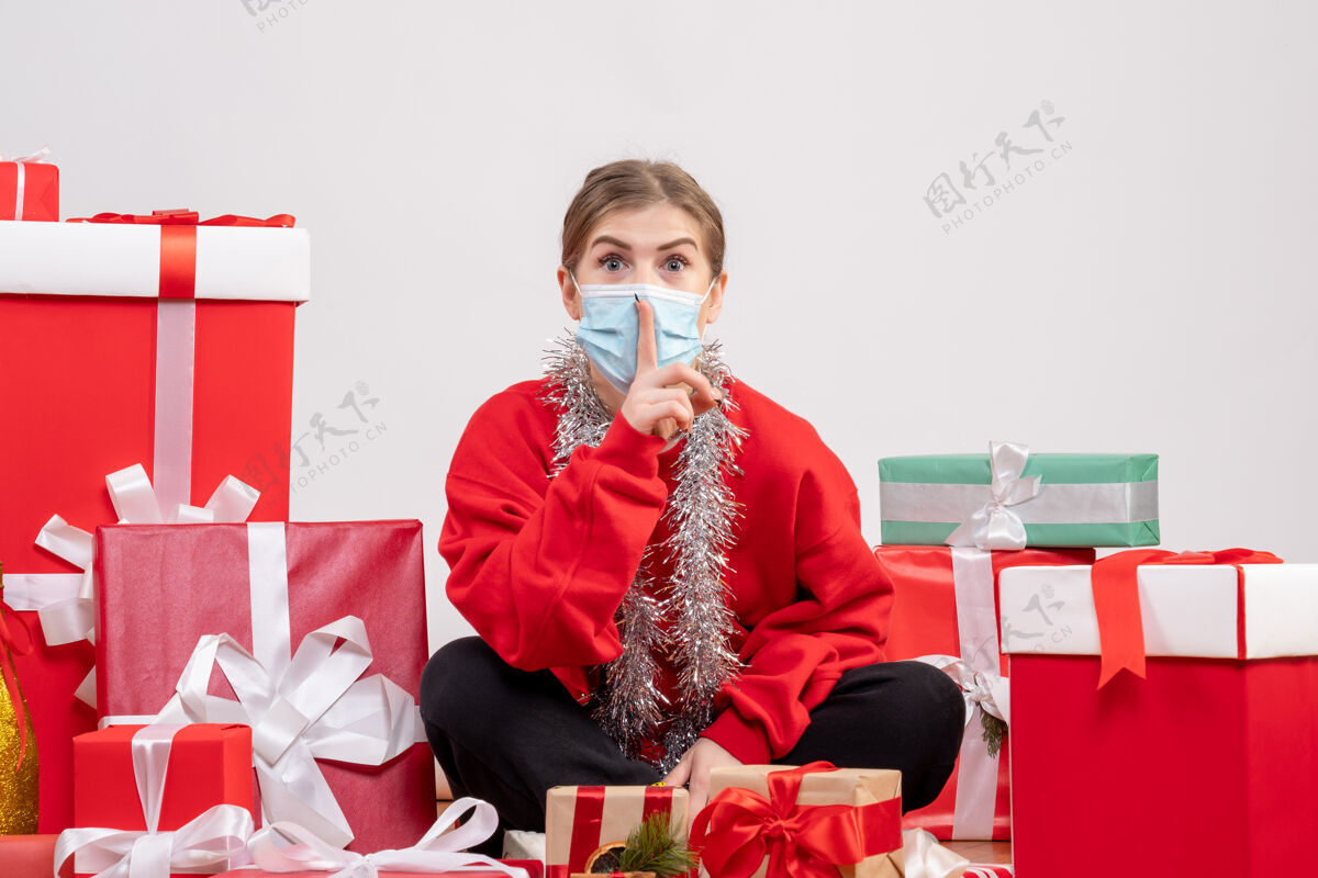 坐着正面图：年轻女性戴着无菌面具坐着 手里拿着圣诞礼物病毒圣诞节礼物