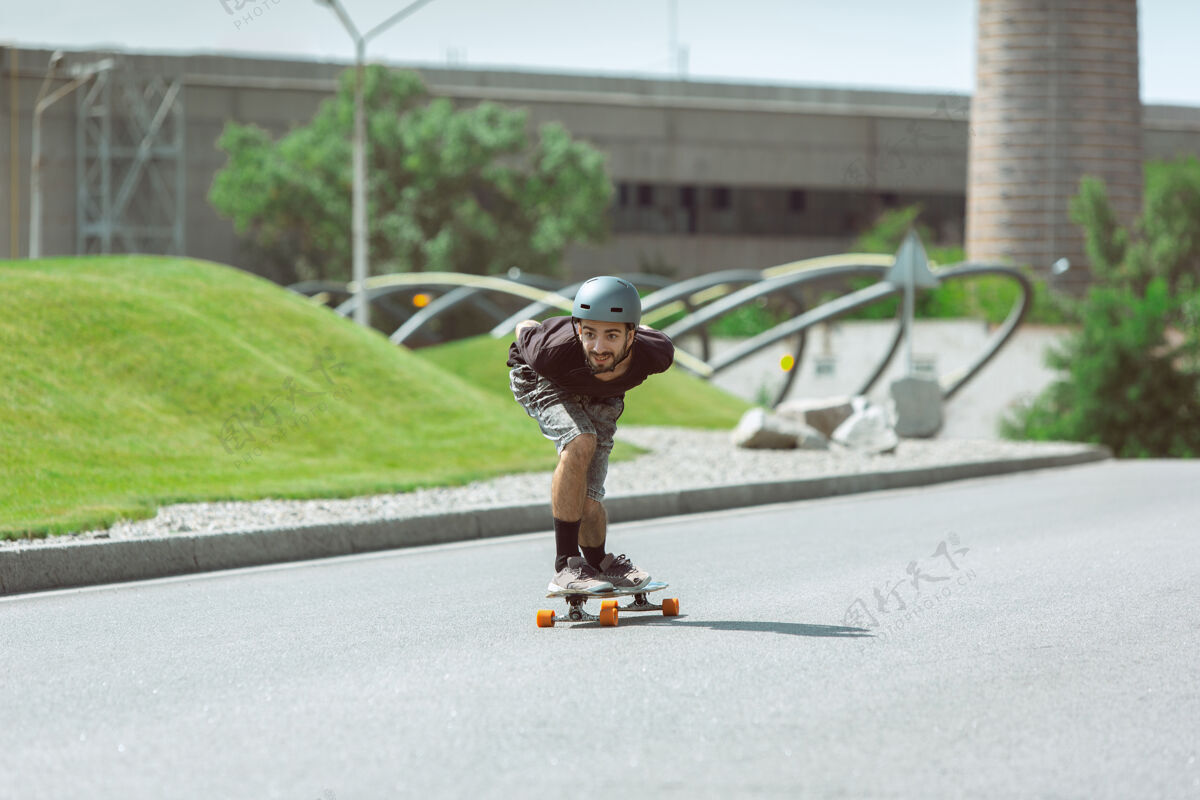 男孩在阳光明媚的日子里 在城市街道上玩滑板的人穿着装备的年轻人在沥青路面上骑行和玩长板休闲活动 运动 极限 爱好和运动的概念游戏平衡年轻