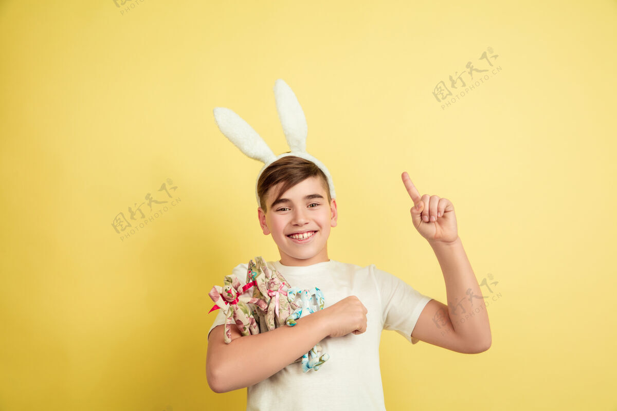 黄色白人男孩作为复活节兔子在黄色工作室背景光明狩猎表情