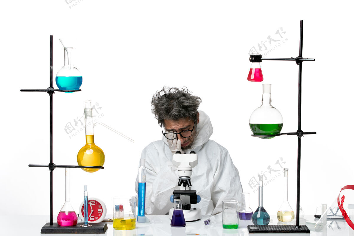 特殊前视图穿着特殊防护服的疯狂男科学家围坐在桌子旁 拿着解决方案对着白色背景的实验室疾病冠状病毒科学病毒哭泣坐着容器实验室