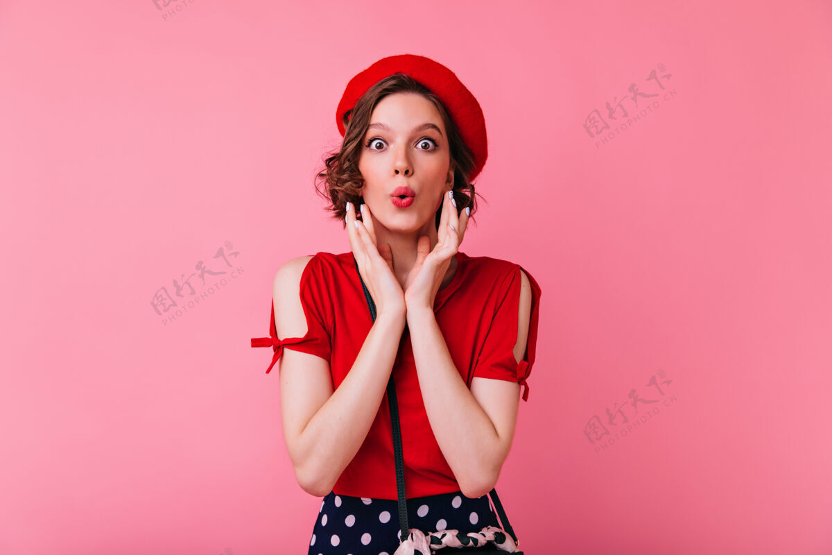 放松穿着红色上衣的漂亮白人女孩摆出亲吻的表情穿着贝雷帽站着的浪漫的法国女人贝雷帽女性粉色