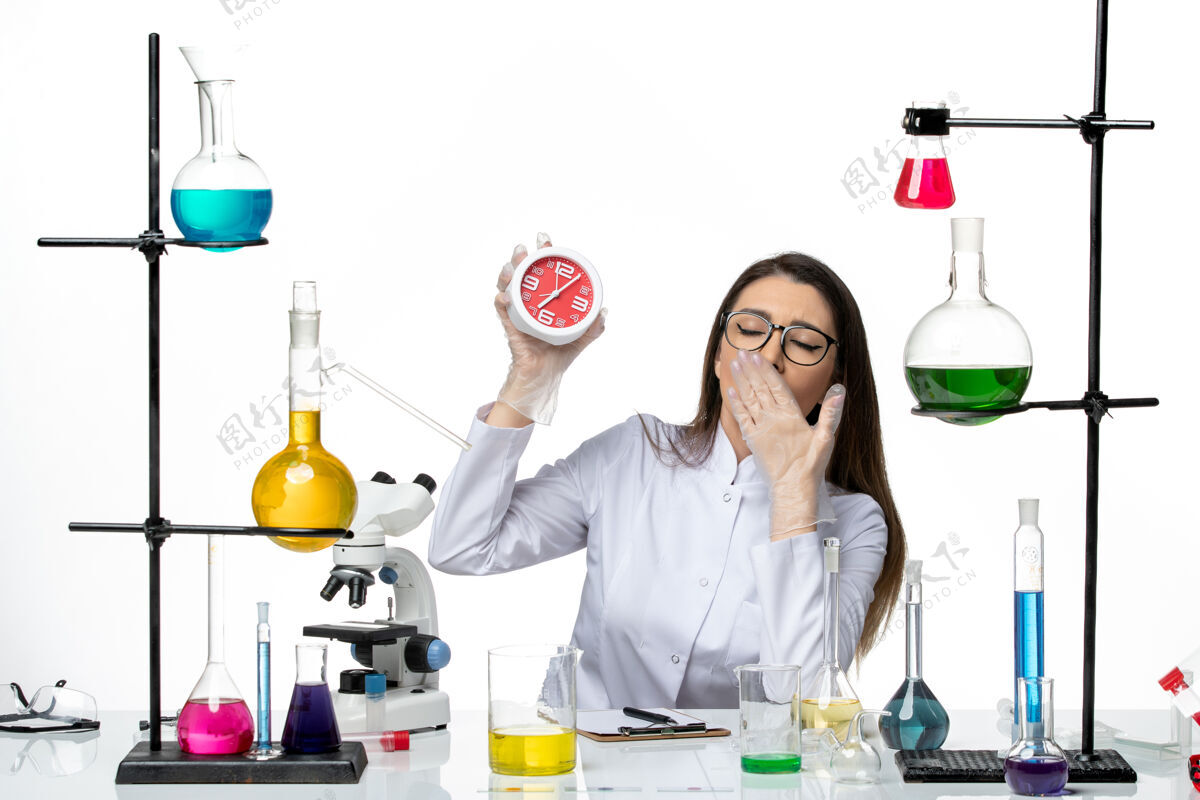医学前视图穿着白色医疗服的女化学家拿着白色背景上的时钟科学病毒实验室柯维德大流行医学大流行科学