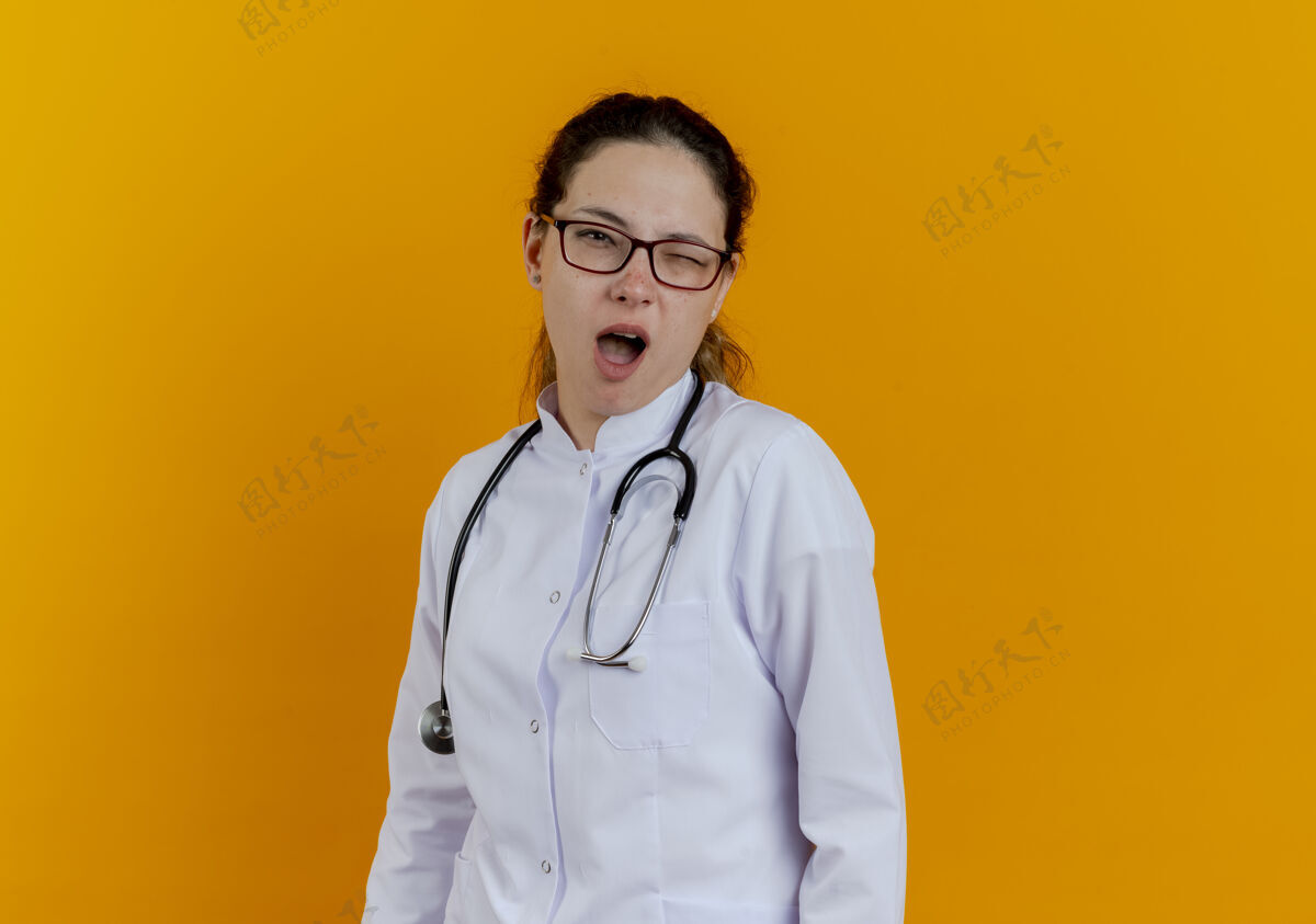 眨眼眨眼的年轻女医生穿着医用长袍和听诊器 戴着隔离眼镜女性橙色女士
