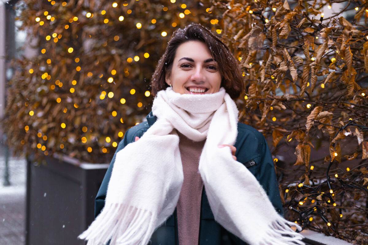 街道高加索快乐微笑的女人享受着雪和冬天 戴着温暖的围巾城市光温暖的衣服